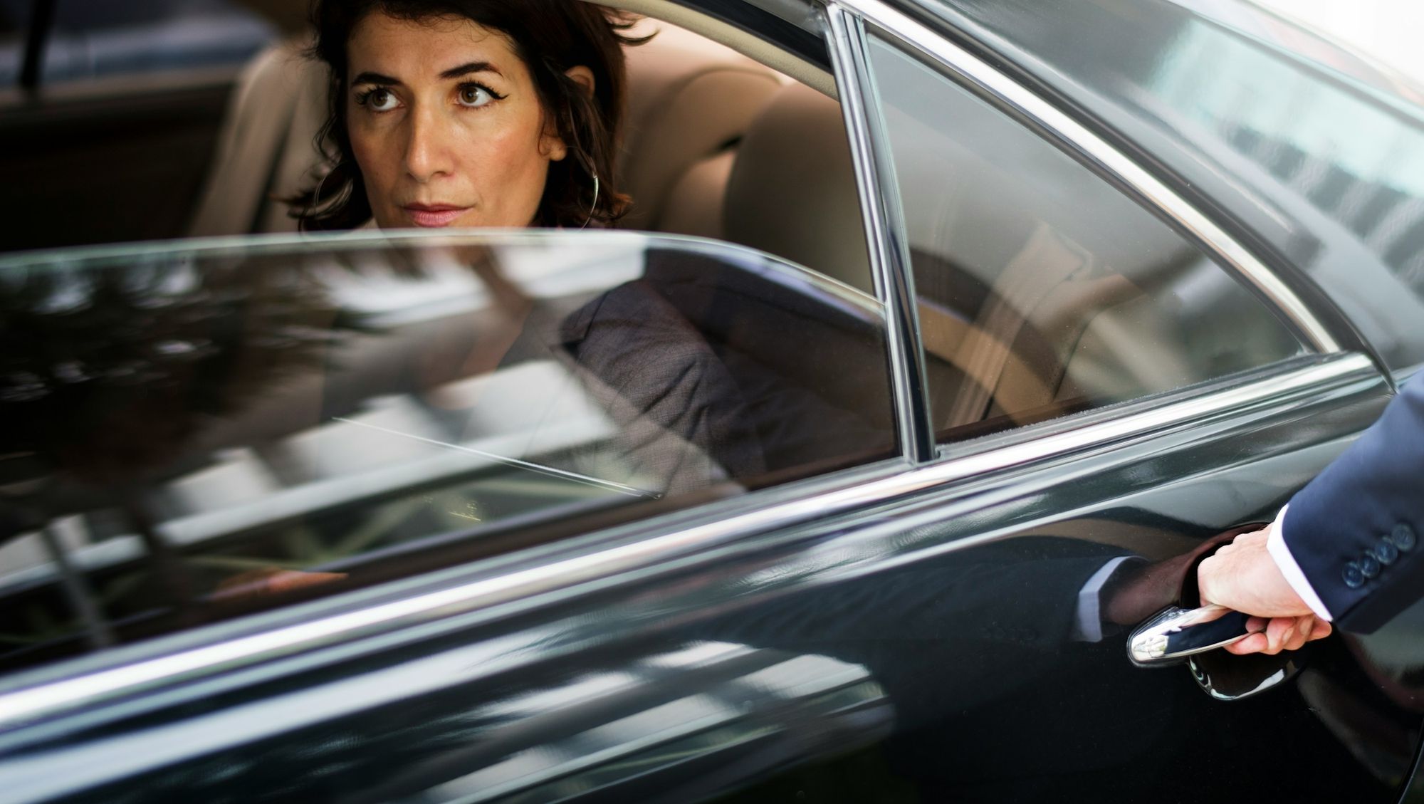 Chauffeur opening the rear door of a black Mercedes for a passenger